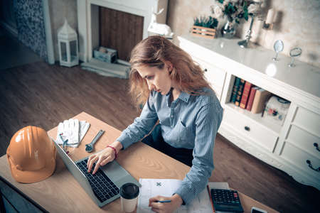 Engineer or Architect Worker Woman is Working at Home Workplace, Portrait of Female Engineer Using CAD on Laptop While Sketch Drawing on Blueprint at Home office. Engineering Occupation Conceptの写真素材
