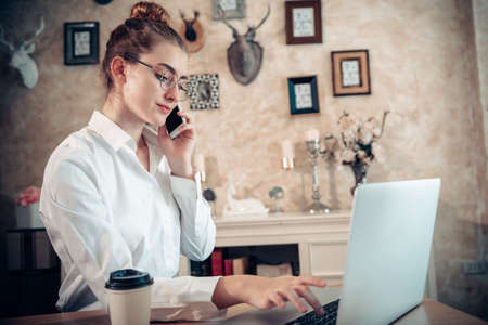 Business Entrepreneur Woman is Working on Table Desk While Calling on Mobile Phone for Own Business in Her Home Office, Businesswoman Worker Busy Work at Home During Covid-19 Pandemic.の写真素材