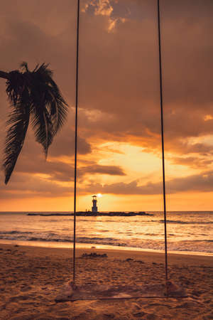 Seascape Scenery View With Empty Swing During Dramatic Cloudy at Sunset, Nature Landscape Tropical Seashore Scenic and Beautiful Beach Against Lighthouse and Horizon Over Background. Relax Vacationの写真素材