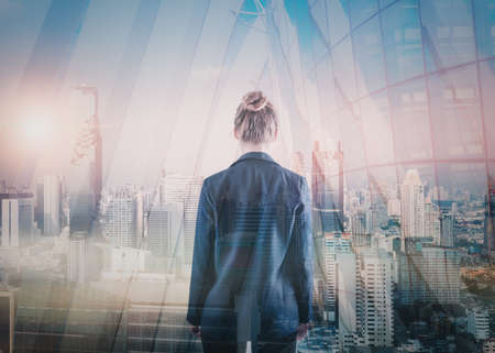 Business Property Development and Investment Concept, Double Exposure of Businesswoman Rear View and Cityscape Buildings. Goal Business Executive Marketing of Successful Entrepreneurの写真素材