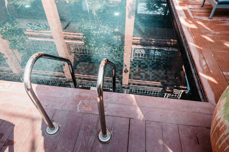 Swimming Pool With Grab Bar Ladder on The Deck Floor, Stair Railing and Terrace Flooring Poolside of Hotel. Outdoor Leisure in Summer Vacation and Lifestyleのeditorial素材