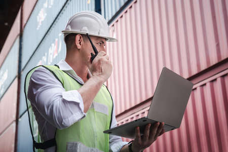 Container Logistics Shipping Management of Transportation Industry, Transport Engineer Managing Control Via Computer Laptop in Containers Shipyard. Business Cargo Ship Import/Export Factory Logistic.の写真素材