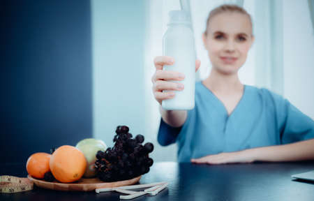 Nutritionist Female Doctor is Showing a Glass of Milk to Camera, Vitamin Nutrients From Vegetables for Healthy Eating. Female Doctor is Consulting and Advise to Patient About Nutrition for Health.の写真素材