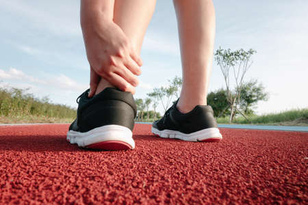 Female Athlete Runner Ankle Injury While Jogging in Running Track, Sport Woman Having Pain Her Ankles During Exercise Running. Sporty Woman Injured Muscle From Workout, Lifestyle and Heath Careの写真素材