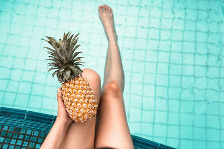 Sexy Woman is Relaxing in Swimming Pool While Holding Pineapple, Close-Up of Beautiful Woman Hold Pineapple and Relax Sunbathe in Poolside on Summer Holiday at Resort Hotel. Summer Vacation Lifestylesの写真素材