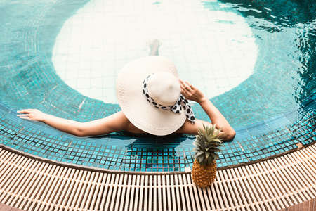 Sexy Woman in Swimsuit is Relaxing in Swimming Pool, Beautiful Woman Wearing Straw Hat and Relax Sunbathe in Poolside on Summer Holiday at Resort Hotel. Summer Vacation and Relaxation Lifestylesの写真素材