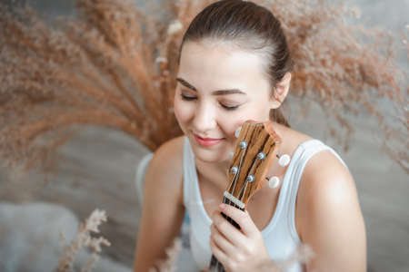 Close-Up Portrait of Pretty Woman is Playing Ukulele in Living Room, Happy Caucasian Woman Relaxing and Happy Emotion With Her Music Instrument. Leisure Activities and Relaxation Entertainment Conceptの写真素材