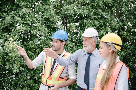 Construction Engineers Team are Discussion and Brainstorming for Project Planning Together, Engineering Teamwork in Safety Equipment are Pointing to Erection Site for Inspection Work Togethernessの写真素材