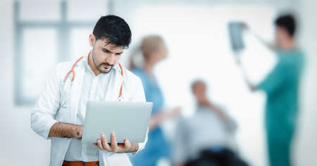 Male Medical Doctor is Using Laptop for Examining Patient in Examination Room, Physician Doctor is Communicating on Laptop While Visiting Diagnosis Patients. Medicine Services/Communication Conceptの写真素材