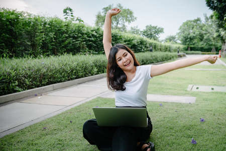 Beautiful Woman Relaxing and Using Laptop While Sitting on Grass Field, Asian Woman Working Online on Laptop Device and Joying 
Social Media. Relaxation Leisure Activities Lifestyles/Work at Homeの写真素材