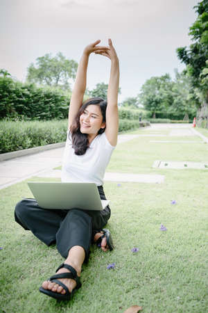 Beautiful Woman Relaxing and Using Laptop While Sitting on Grass Field, Asian Woman Working Online on Laptop Device and Joying 
Social Media. Relaxation Leisure Activities Lifestyles/Work at Homeの写真素材