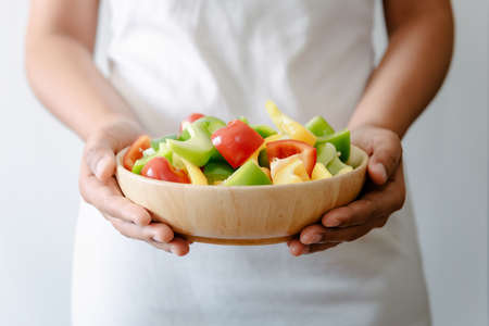 Sweet Pepper Vegetable, Female Hands Chef Holding Bowl of Mixing Sweet Pepper. Woman Hands Holding Salad Bowl During Preparation for Cooking in The Kitchen. Fresh Sweet Peppers Vegetables for Healthyの写真素材
