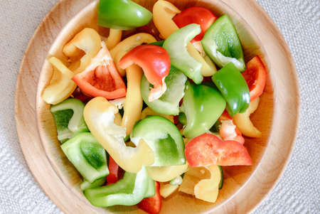 Sweet Pepper Cutting Sliced Preparation for Cooking. Raw Variety Red, Green, Yellow Sweet Peppers Slicing Chopped in Wooden Bowl on Kitchen Table. Raw Organic Sweet Pepper Ready to Eatの写真素材
