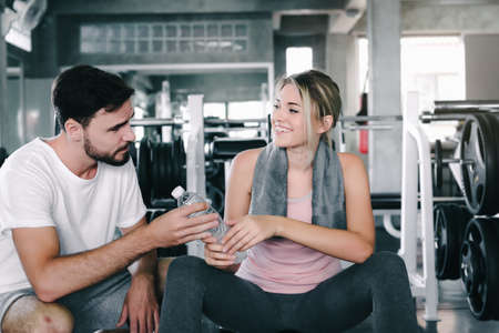 Sport Couple Love Sharing a Bottle of Water Together After Exercised in Fitness Club, Attractive Sporty Young Couple Enjoy Exercising Together in Fitness Gym. Exercise Training and Sport Lifestyles.の写真素材
