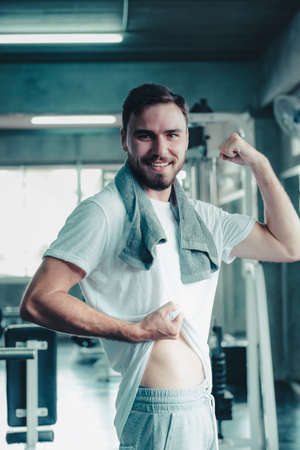 Sport Fitness Man Standing Poster With Body Muscular After Exercise in Fitness Gym. Portrait of Confident Sport Young Male Posting Body Muscle Shape in Exercising Gym Training Room. Body Health Careの写真素材