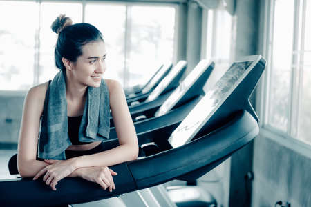 Sporty Woman in Sportswear is Resting Tired During Exercise on Treadmill Machine in Fitness Gym, Smiling Asian Woman Exercising Treadmill Running Machines in Fitness Club. Sport Exercises Trainingの写真素材