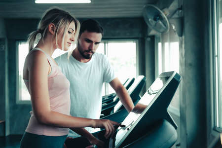 Sporty Woman in Sportswear is Exercising Training on Treadmill Machine With Her Trainer in Fitness Gym, Sport Woman Exercised on Treadmill Running Machines in Fitness Club. Sport Exercises Trainingの写真素材