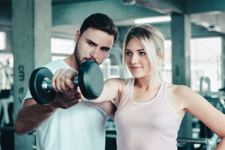 Sporty Woman is Exercising Train While Lifting Dumbbell With Her Trainer in Fitness Room, Sport Woman Having Exercised Workout Training With Male Trainer Together in Fitness Club. Sport Lifestylesの写真素材