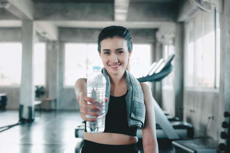 Sport Fitness Exercise and Healthy Lifestyle, Attractive Sports Woman Drinking a Bottle of Water During Taking Rest Break in Fitness Club. Leisure Lifestyles and Exercise Training in Fitness Gym.の写真素材