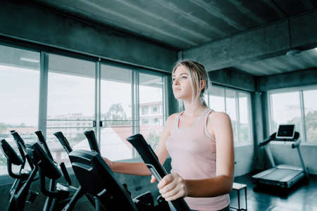 Sporty Woman is Exercising in Fitness Club, Female Sport in Sportswear Workout Exercised on Fitness Machine. Portrait of Attractive Athlete Woman Exercising Training Class in Fitness Gymの写真素材