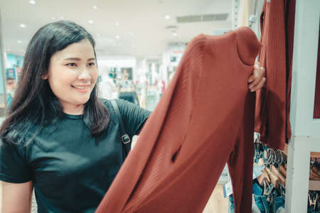 Promotion Sale and Clothes Shopping Concept, Shopaholic Woman is Looking for Choosing Clothes in Shopping Department Store. Attractive Woman Enjoying While Shopping in Mall Shop. Leisure Lifestylesの写真素材
