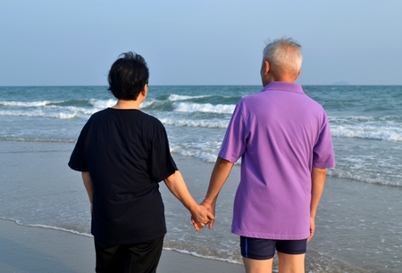 Asian old couple holds hand along the beachの写真素材