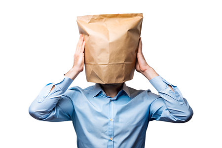 A man wearing a blue button-up shirt holds a crumpled piece of paper in his hand. He is standing in a room with a window in the background.の写真素材