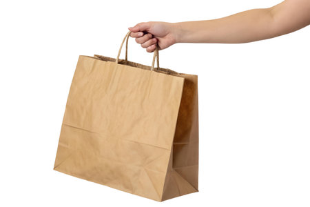 Close-up of a hand holding a light brown paper shopping bag against a black background.の写真素材