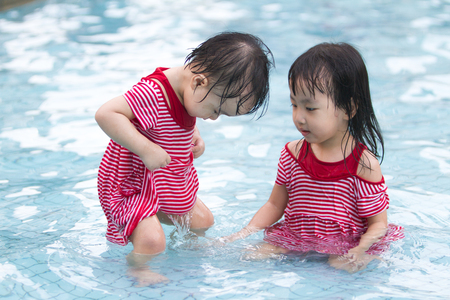 Two Little Sisters Playing in Water in Swimming Poolの写真素材