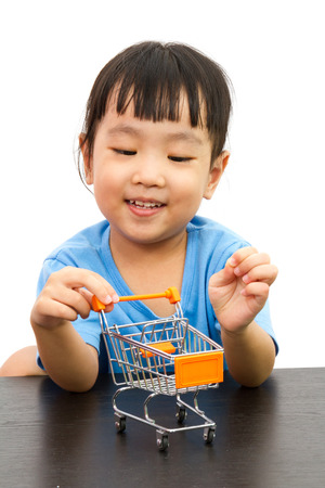 Chinese little girl pushing a toy shopping cart in plain white isolated background.の写真素材