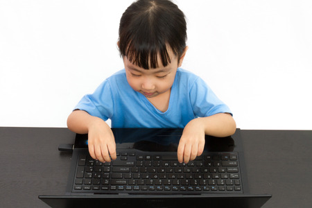 Chinese little girl using laptop in plain isolated white background.の写真素材