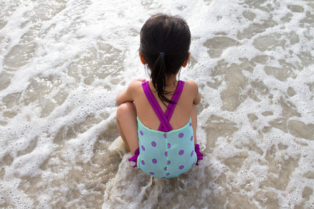 Asian Little Chinese Girl Sitting on the Beach Wearing Swimsuitの写真素材