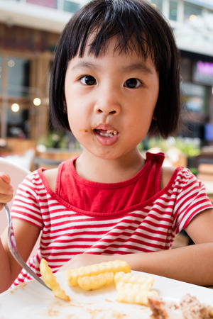 Asian Little Chinese Girl Eating French Fries in Outdoor Cafeの写真素材