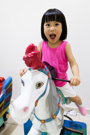 Asian Little Chinese Girl Riding on a Horse in Indoor Playgroundの写真素材