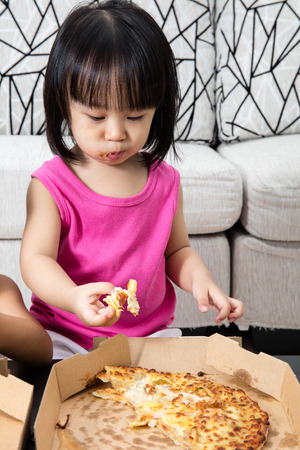 Asian Little Chinese Girl Eating Pizza at Homeの写真素材