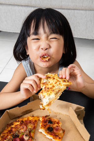 Asian Little Chinese Girl Eating Pizza at Homeの写真素材