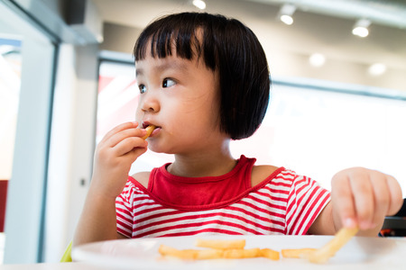 Asian Chinese little girl eating french fries at restaurant.の写真素材