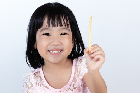 Happy Asian Chinese little girl Eating French Fries at indoor isolated clean background.の写真素材