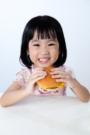 Asian Chinese little girl Eating Burger indoor with isolated clean background.の写真素材