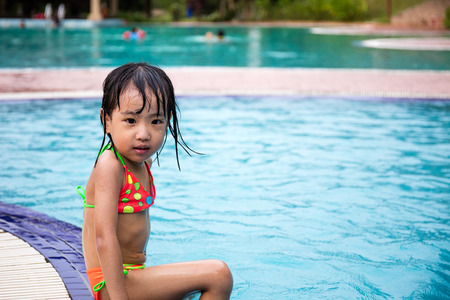 Asian Chinese Little Girls Sitting At The Edge Of Outdoor Swimming Pool.の写真素材