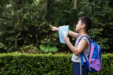 Asian Chinese little boy holding map pointing in the forest looking for direction.の写真素材
