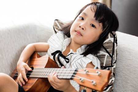 Asian Chinese little girl sitting at the sofa playing ukele.の写真素材