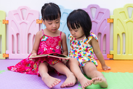 Asian Chinese little sisters sitting on the floor reading at homeの写真素材