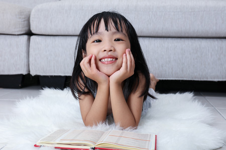 Happy Asian Chinese little girl reading book on the floor in the living room at home.の写真素材