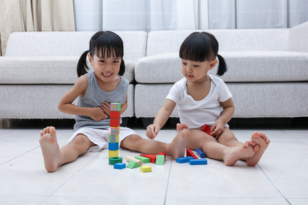 Happy Asian Chinese little sisters playing blocks on the floor in the living room at home.