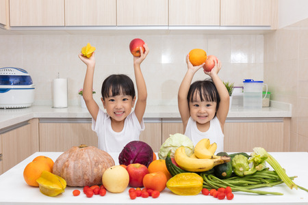 Happy Asian Chinese little sisters with fruit and vegetable in the kitchen at homeの写真素材