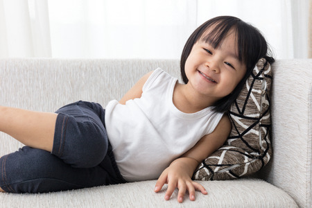 Happy Asian Chinese little girl lying down on the sofa in the living room at home.の写真素材