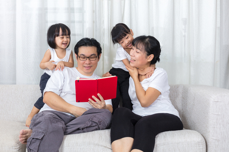 Happy Asian Chinese family reading book on the couch in the living room at home.の写真素材