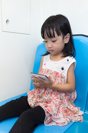 Asian Chinese little girl sitting inside a MRT with a mobile phone in Kuala Lumpur City, Malaysia.の写真素材