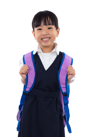 Happy Asian Chinese little girl wearing primary school uniform with school bag in isolated white background.の写真素材